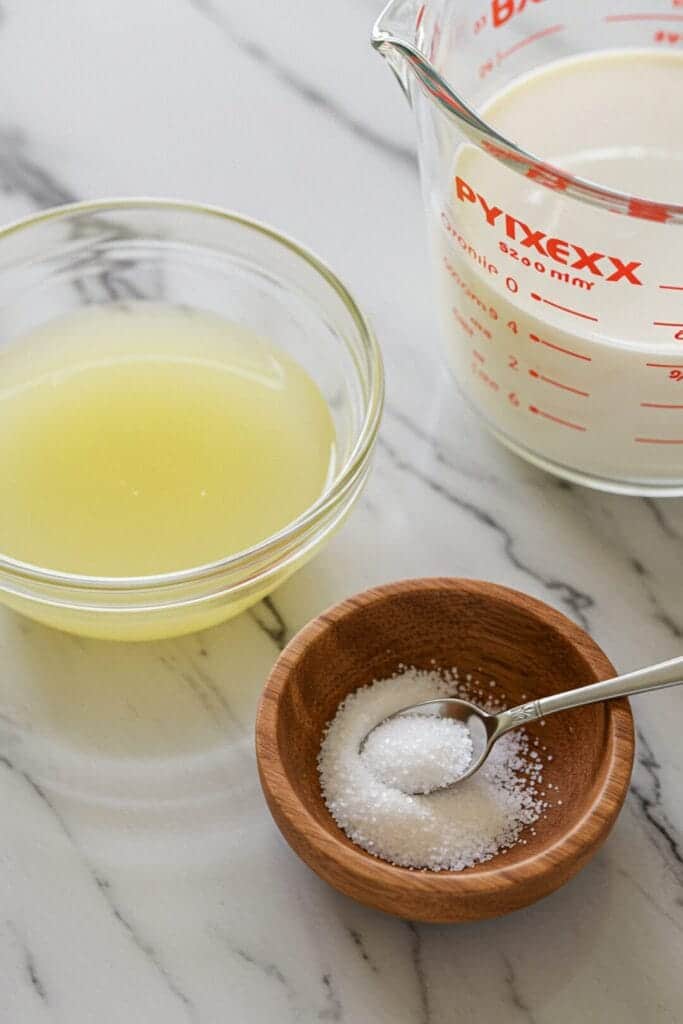 Cream cheese recipe ingredients: Milk, lemon juice, and salt on a wooden countertop, ready for homemade cream cheese.