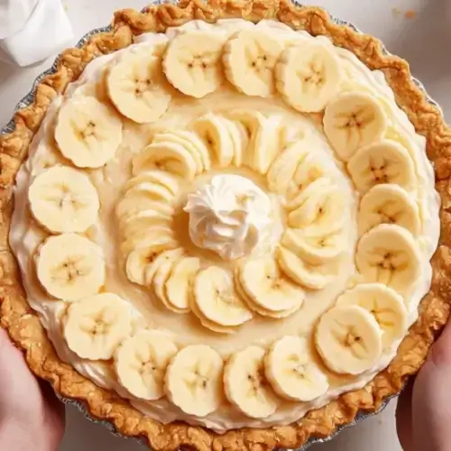 Easy Cream Pie Recipe topped with fresh banana slices and whipped cream in a golden flaky crust