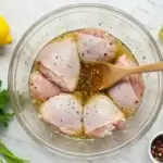 Chicken thighs marinating in homemade Lemon Pepper Chicken Marinade with lemon, garlic, peppercorns, and olive oil.