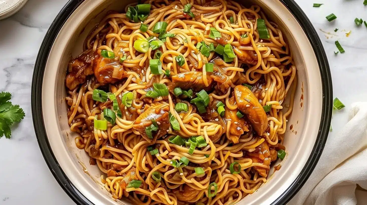 Crockpot sticky garlic chicken noodles served in a bowl with herbs